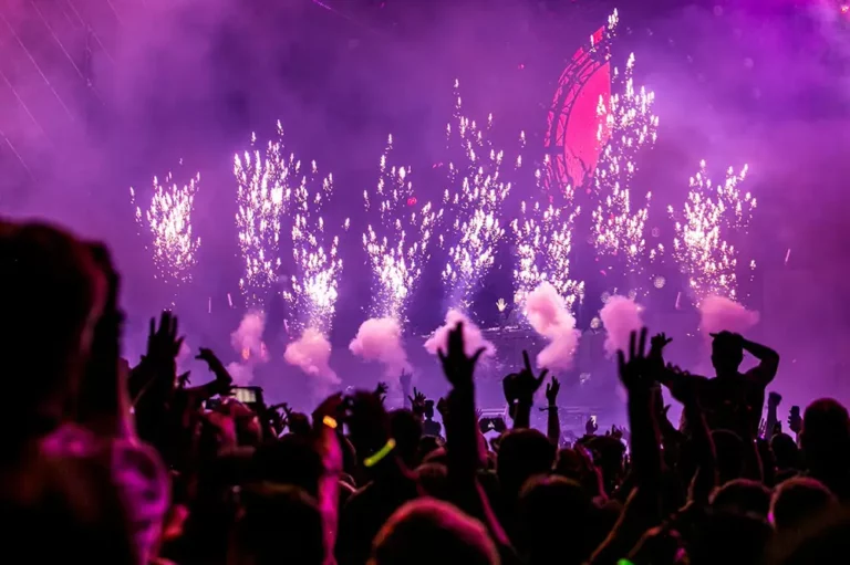 Spectacular live concert scene in Ibiza, enhanced by Avcon Jet services, with vibrant purple fireworks illuminating the night sky above a crowd of enthusiastic concert-goers.