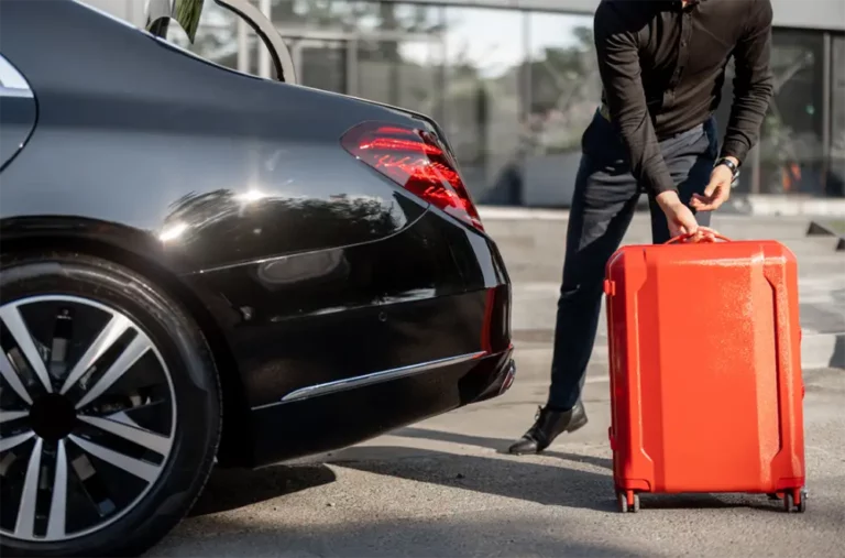 Avcon Jet's premium concierge service in Ibiza, showing a staff member placing a bright red suitcase into a luxurious black sedan, preparing for a guest's seamless travel experience.
