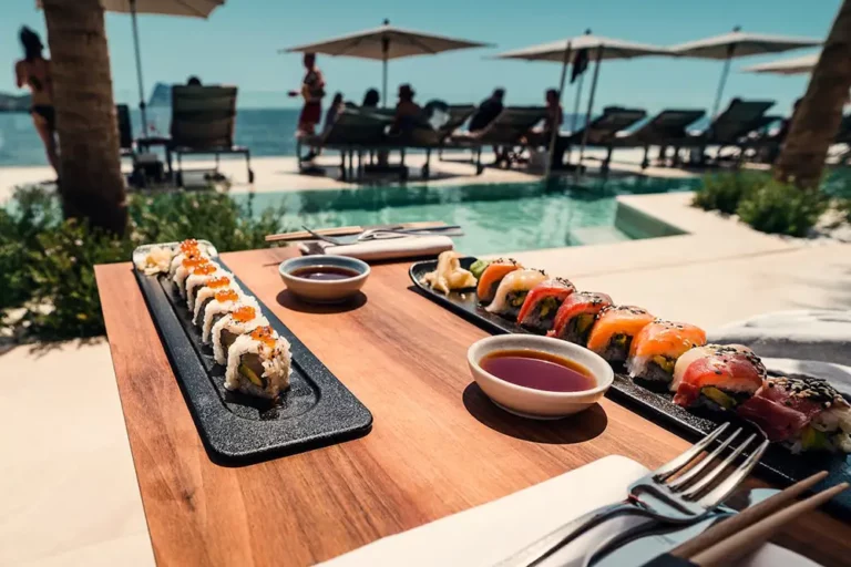 Enjoying exquisite sushi at a luxury poolside setting in Ibiza, catered by Avcon Jet, with assorted rolls including salmon and avocado on a sleek black serving plate, accompanied by soy sauce, with resort guests lounging in the background.