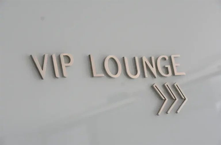Chic VIP lounge entrance in Ibiza with a minimalist 'VIP LOUNGE' sign, indicating an exclusive area facilitated by Avcon Jet, featuring stylish arrow symbols pointing right.
