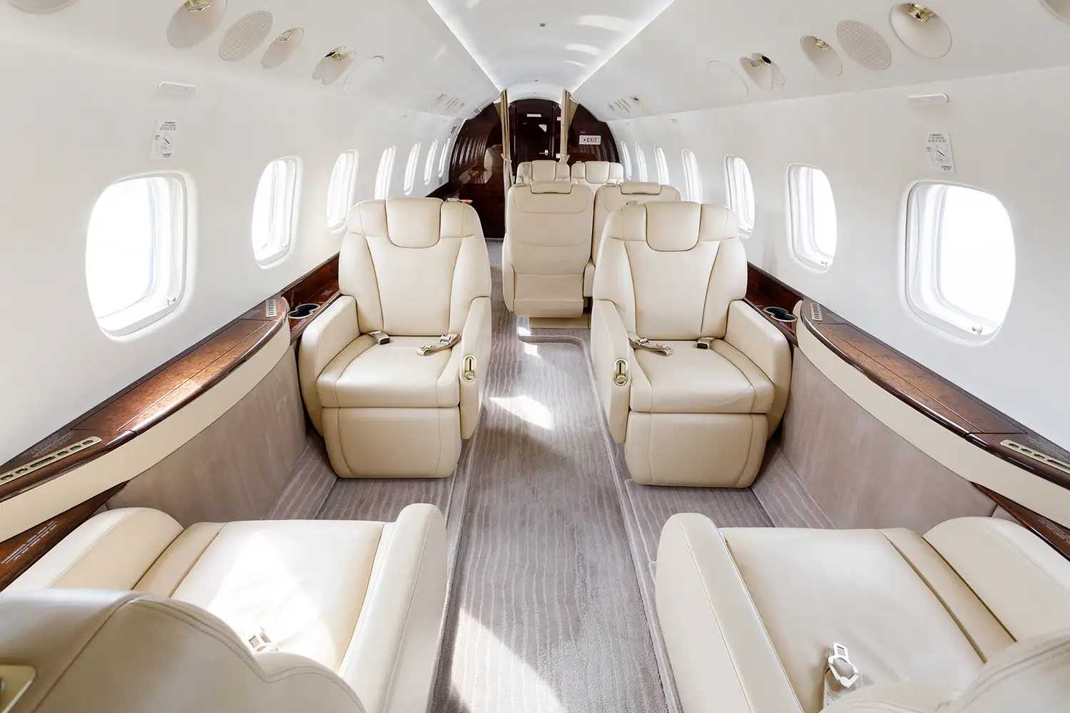 Interior of a luxurious business jet, ideal for empty leg flights, featuring spacious beige leather seats aligned along both sides of the cabin, with ample natural light from the oval windows and a polished wood trim for an elegant finish.
