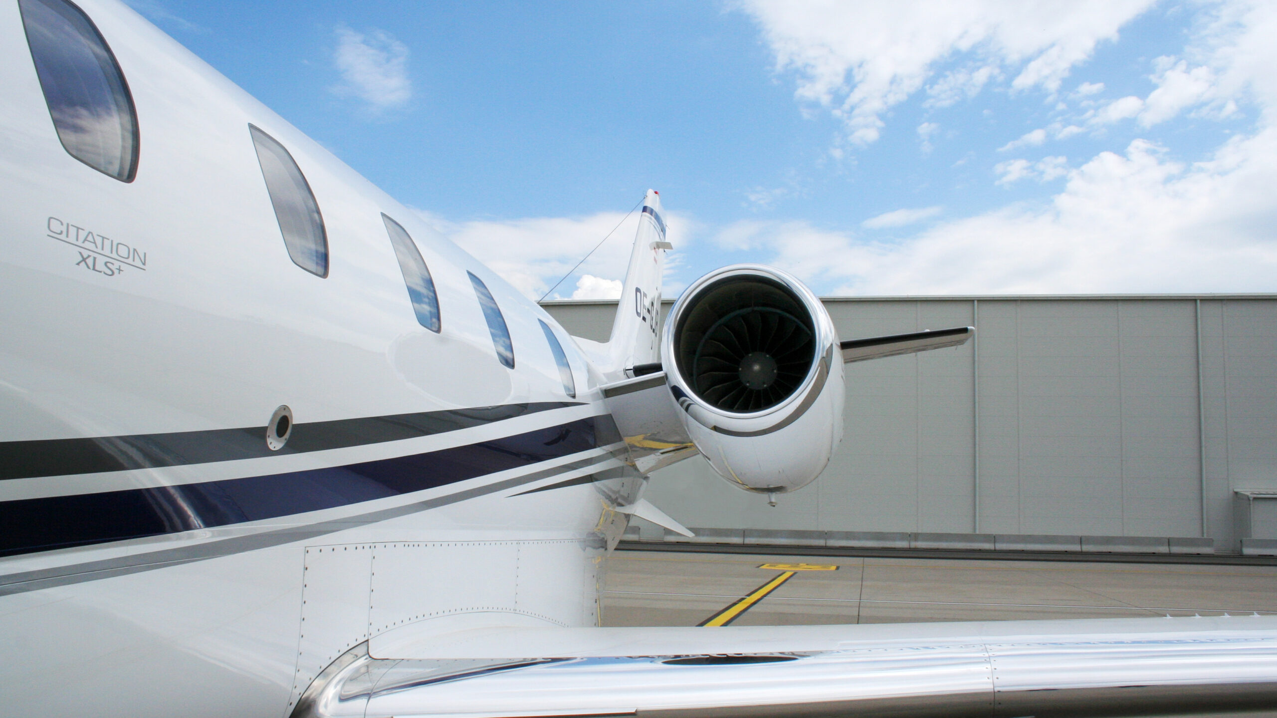 Cessna Citation XLS+ with a grey and blue painting standing on the Apron in front of a business jet hangar