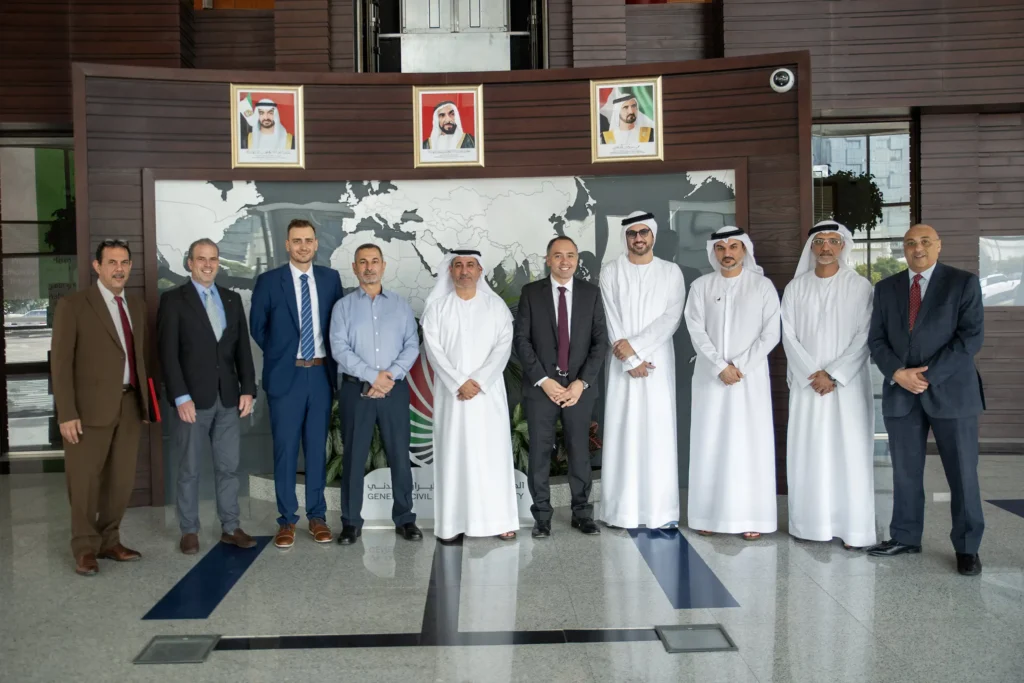A group of ten aviation officials and executives pose together in the General Civil Aviation Authority lobby. They stand beneath framed portraits and in front of a large world map wall with part of the authority sign visible.